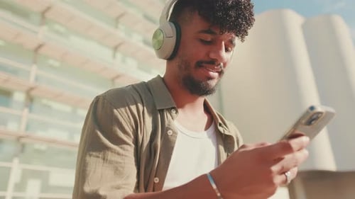 Close up, young student sits outside next to the university, listens to music on headphones