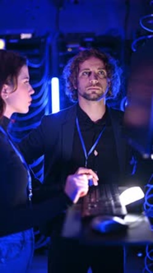 Man and Woman Collaborating in Dark Server Room