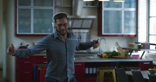 Happy Man Dancing and Singing with Headphones in Kitchen