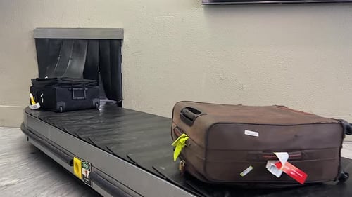 Suitcases emerge from passage in wall on airport luggage carousel