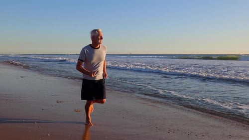 64 year old man jogging at the beach. Slow Motion.