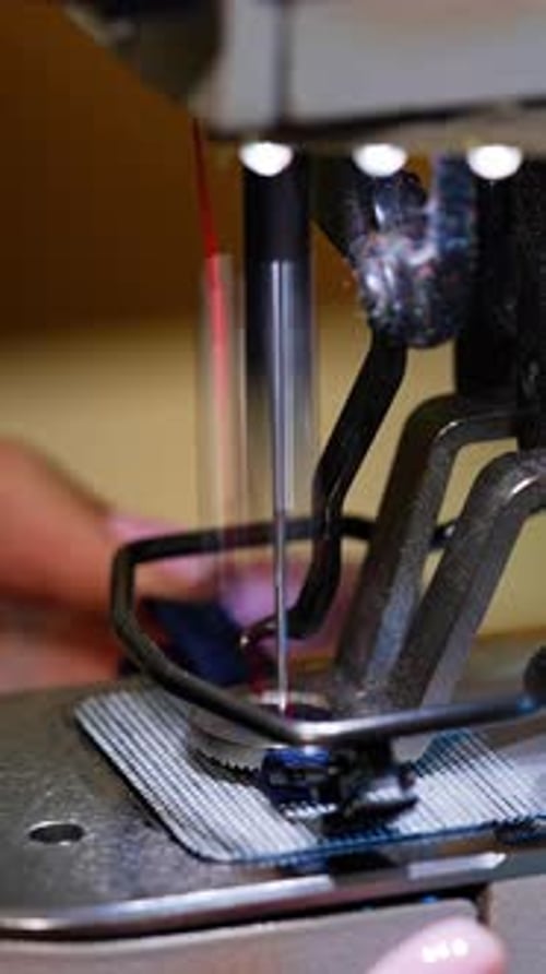 Woman using sewing machine in factory. Female hands working on tailoring industrial fabric.