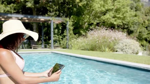 Relaxing by pool, woman in sunhat using tablet, enjoying summer day, copy space