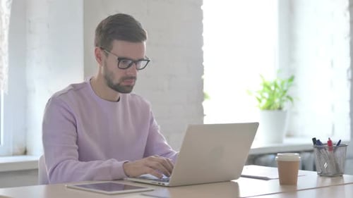 Stressed Man Working on Laptop in Bright Office
