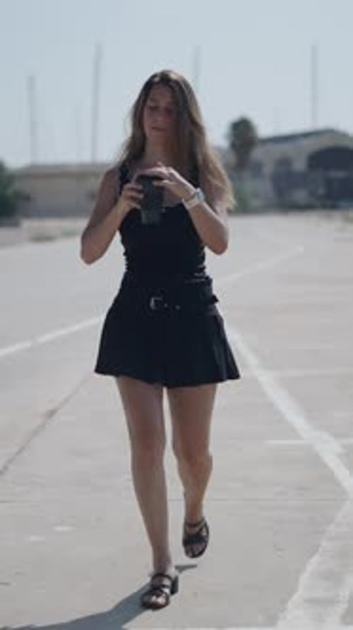 Young Girl Caucasian Woman in Short Black Dress Walking Facing Camera in Suburban Industrial Area