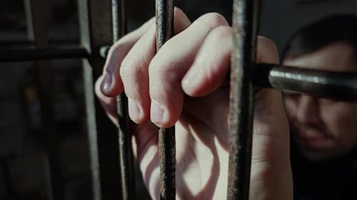 Male Hand Gripping Cold Prison Cell Bars