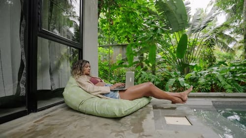 Woman Relaxing Outdoors in Tropical Beanbag Chair With Laptop