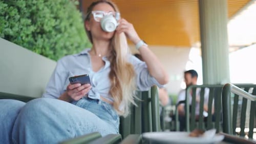 Woman Drinking Coffee and Using Smartphone at Cafe