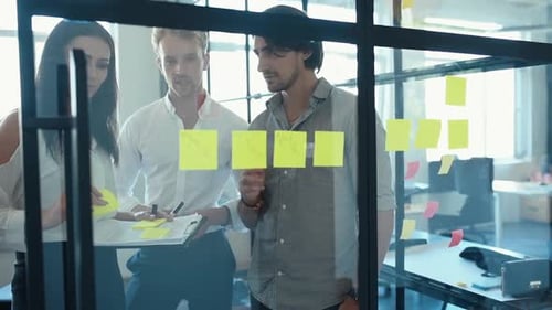 Young business people in formal clothes planning work in the office with paper stickers on the glass