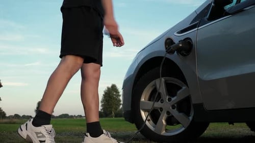 Man Unplugs Electric Car in Rural Environment