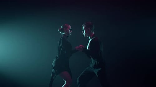 Sensual latino dancers performing passionate ballroom dance in dark hall spotlight