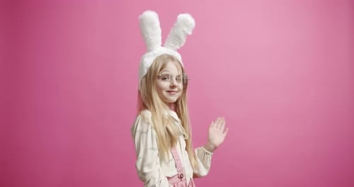 Girl Wears Bunny Ears and Waves on Pink Background