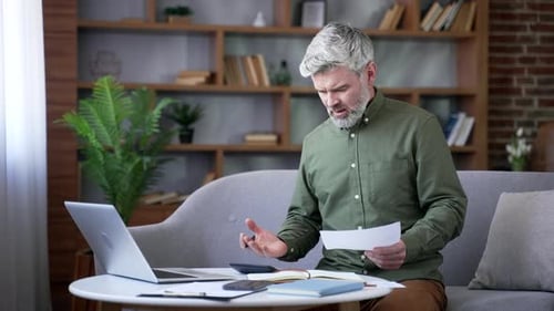 Man Looks at Bills with Frustration in Living Room
