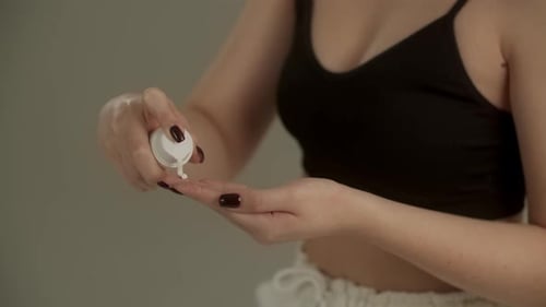 Cropped View of Woman Squeezing Cream From Tube Onto Her Fingers A Woman in a Black Tank Top Stands