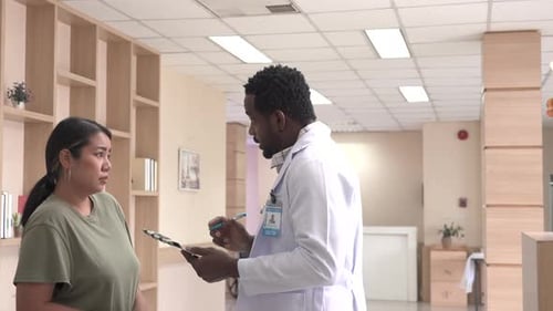 African doctor talk and hold clipboard through hospital hallway