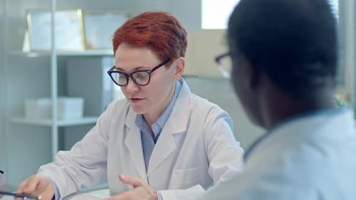 Female Doctor Having Discussion with Coworker on Meeting in Medical Office