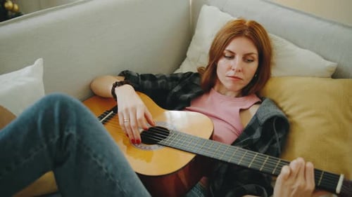 Woman playing guitar while relaxing on couch