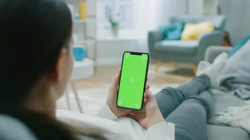 Young Woman at Home Resting on a Couch using with Green Mock-up Screen Smartphone. Girl Using Chrom