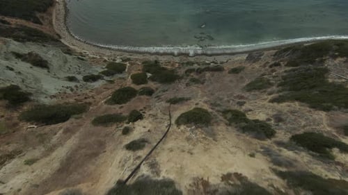 Flying over a cliff toward the ocean and beach and then along the rocky terrain of the coastline - f