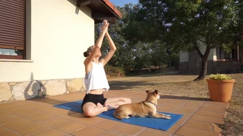 Woman Practices Yoga Next to Dog Outside on Patio