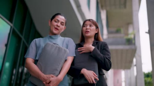 Two happy friendly business woman talking while taking a break standing in the office. Share ideas a