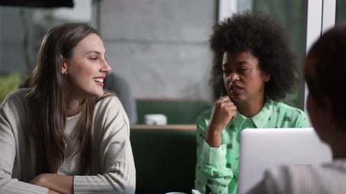Three women brainstorming ideas at coffee shop working remotely with laptop. Female colleagues in