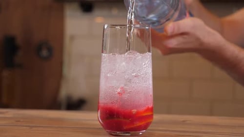 Pouring Liquid Into Glass with Fruit and Ice
