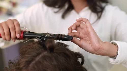 Closeup of Unrecognizable Pretty Woman with Brown Hair Having It Treated with Curling Iron By Female