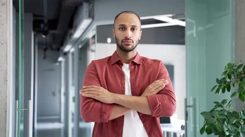 Portrait of serious businessman standing with crossed arms at workplace in a modern business office.