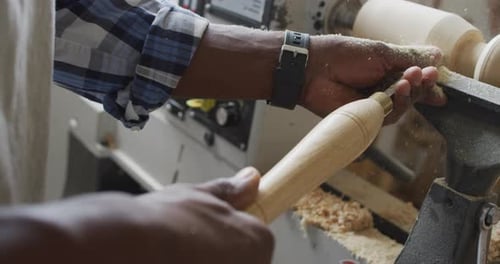 Close up of african american male carpenter hand's turning wood on a lathe at carpentry shop