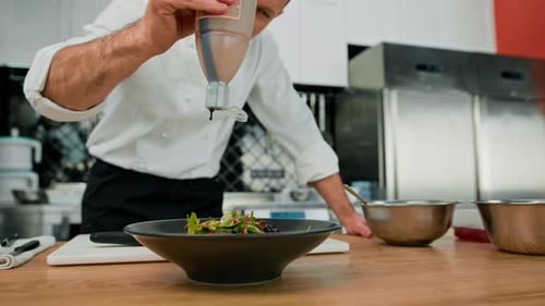 Professional kitchen the chef pours sauce on the salad with pear and cheese mixes the ingredients