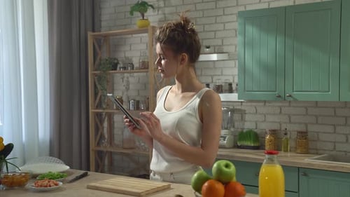 Young Woman at the Table in the Kitchen Preparing Spring Rolls for Healthy Lunch Reading Recipe on