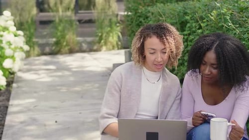 Two smiling women working on laptop outdoors