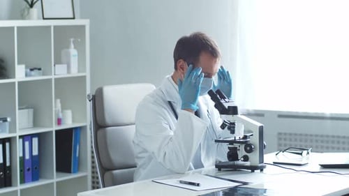 Professional Medical Doctor Working in Hospital Office Using Microscope