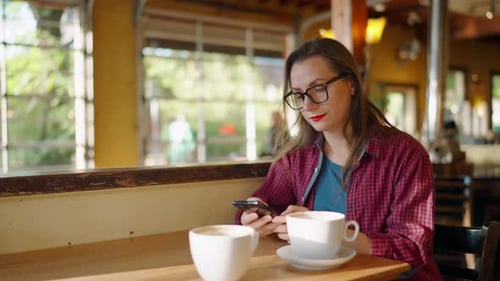 Woman is Using Smartphone and Drinking Coffee in the Cafe