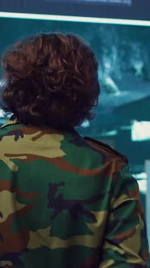 Man in Camouflage Jacket Standing Before Monitor