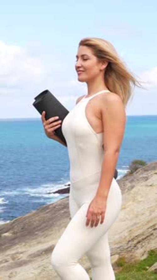 Blonde woman holding yoga mat by the sea