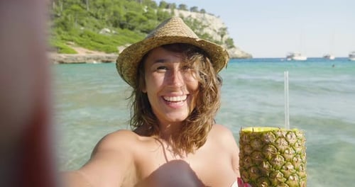 Beautiful young girl doing selfie at sea, drinking pineapple cocktail, in swimsuit in straw hat, b