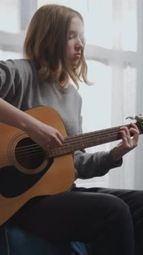 Teen Girl Plays Acoustic Guitar by Window Light