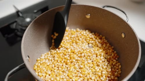 Préparation du pop-corn, les grains sont mélangés dans la casserole sur la cuisinière à gaz.