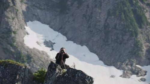 Photographer pivots with camera on tripod on alpine mountain ridge, Tim Durkan medium tracking helic