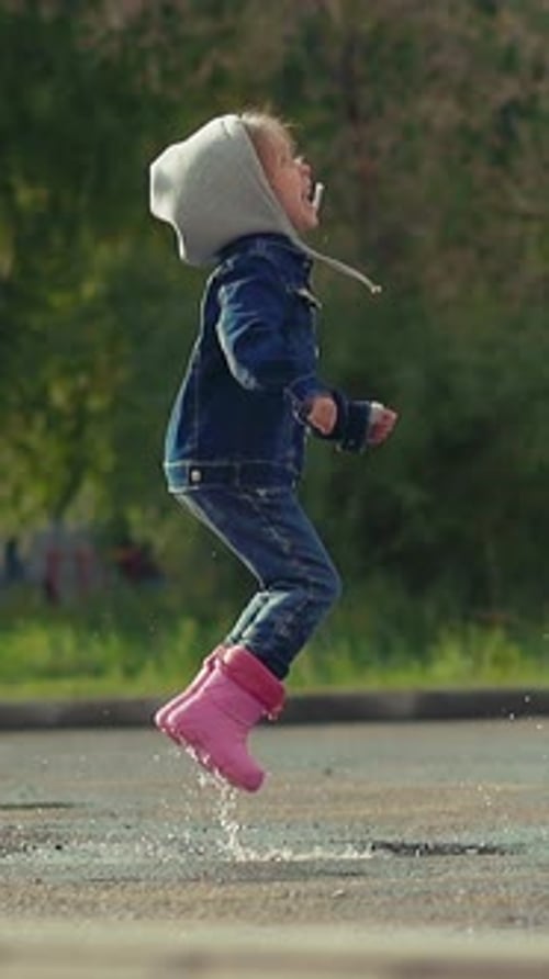 Little Child Happily Jumps in Deep Puddle