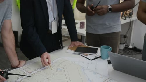 Male Specialists Discussing Blueprints by Table in Construction Office