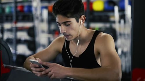 Hispanic Man in Gym Resting, Holding Smart Phone,listening Music Active