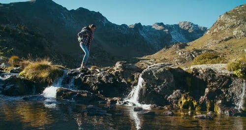 Traveler Woman Crossing Mountain River on Vacation Trip with Hiker Backpack