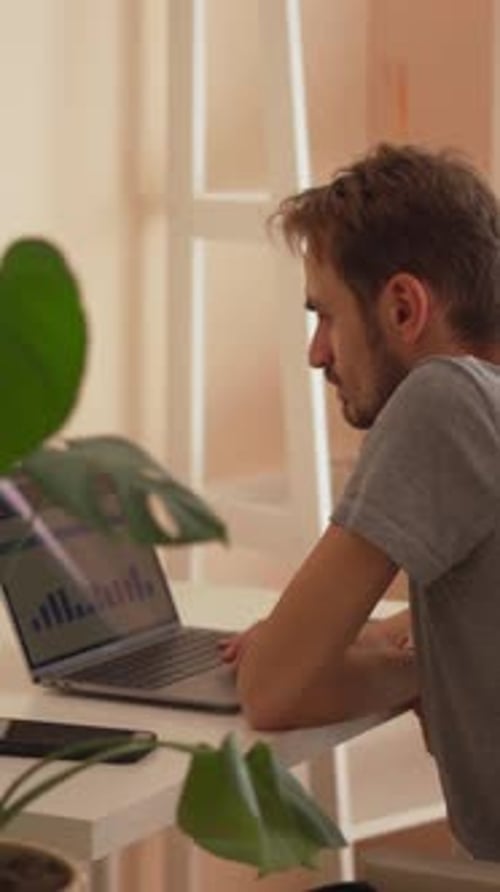 Un jeune homme concentré travaille assidûment sur son ordinateur portable dans un espace de travail lumineux et contemporain conçu
