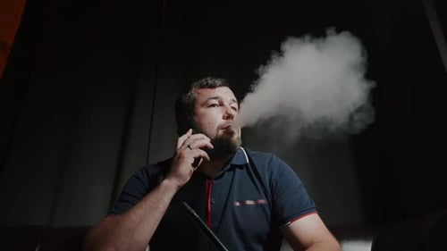 Homme d'affaires assis et écoutant une conversation téléphonique tout en se relaxant dans le salon Hookah en expirant