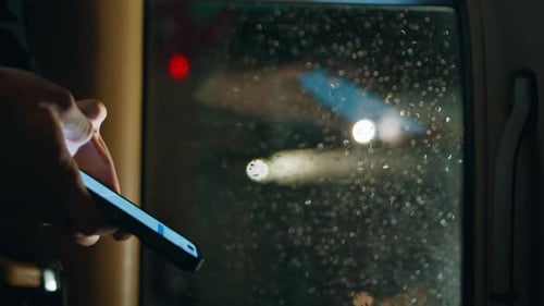 Hand Using Smartphone Next to Rain Window At Night