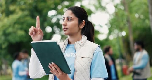 Woman Directing Volunteers in Park with Tablet