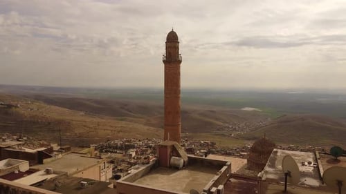 Tall stone minaret overlooking town and distant hills in Mardin Turkey
